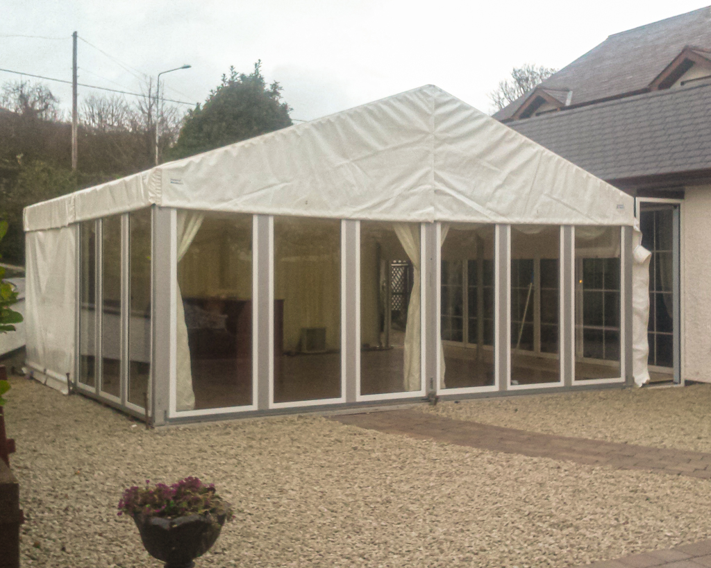 A marquee adjacent to the back of a house with glass siding and a bar inside